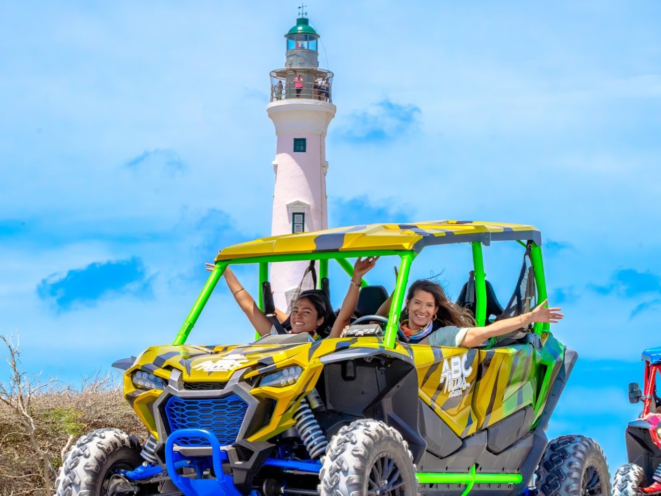 People in off-road vehicle near lighthouse on a sunny day.