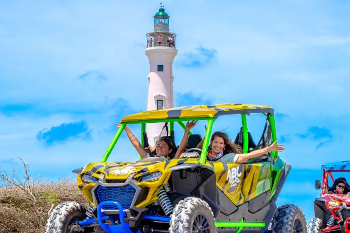 People in off-road vehicle near lighthouse on a sunny day.