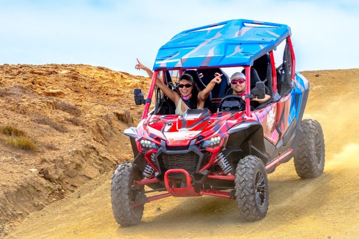 Two people in an off-road vehicle driving on a dirt path.