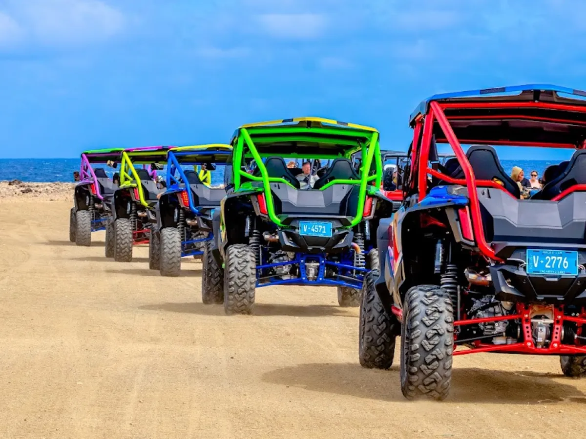 Colorful off-road vehicles driving in a line on a sandy path under a blue sky.