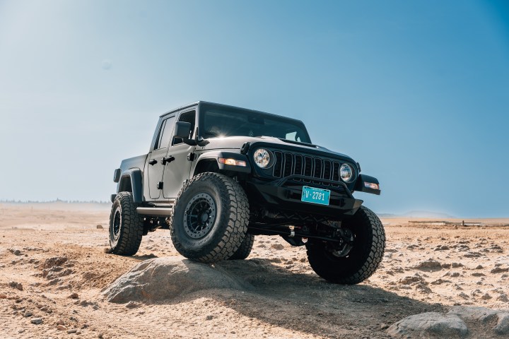 Black off-road vehicle on rocky desert terrain under blue sky.