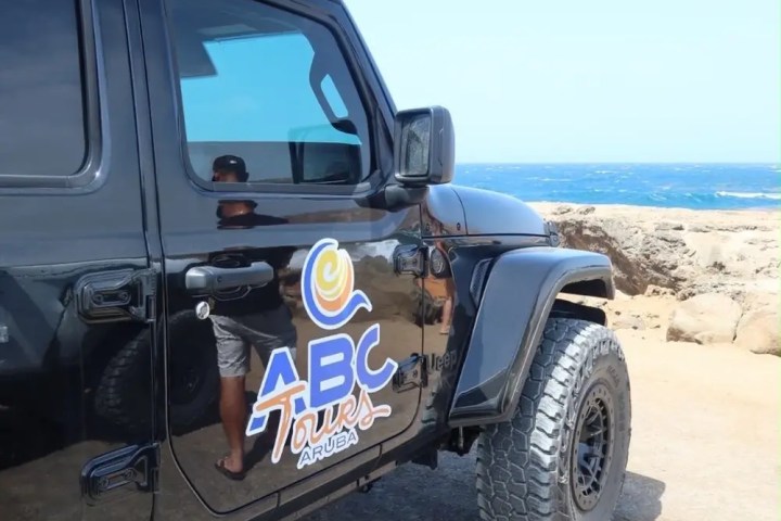 Black off-road vehicle with ABC Tours logo parked by a rocky beach.