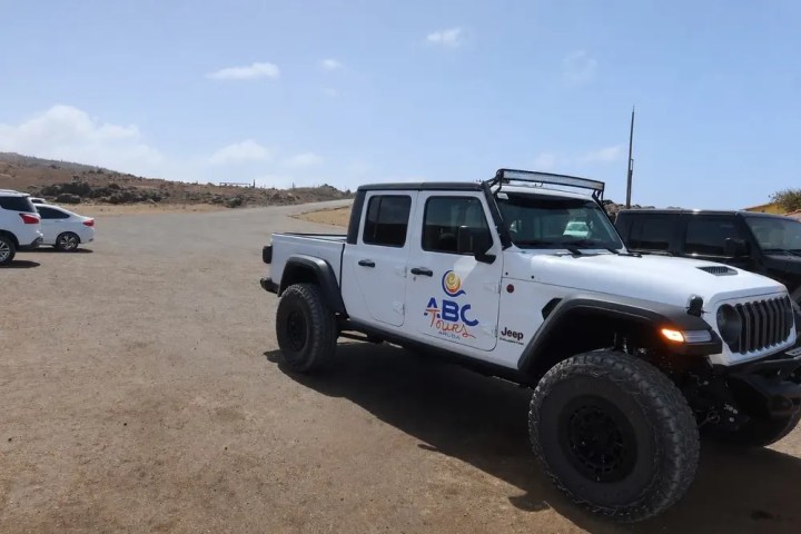 White Jeep truck with ABC logo parked on gravel near other cars.