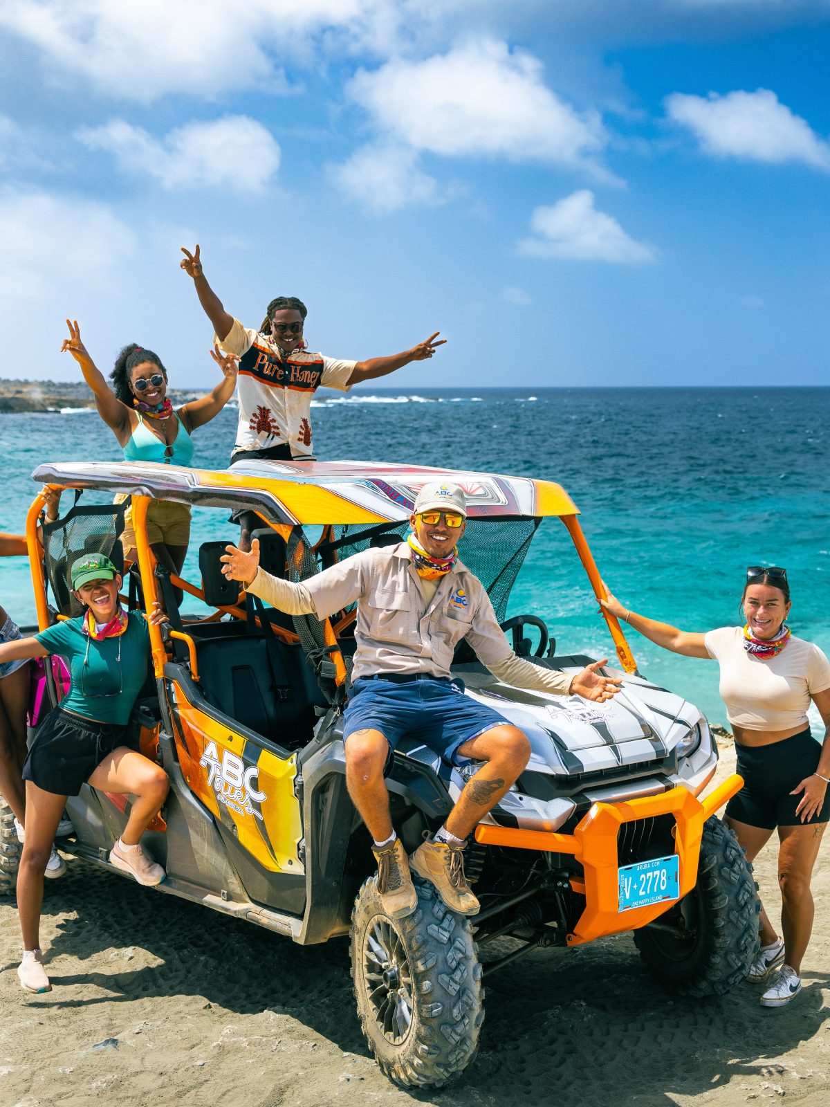 Group posing on a yellow off-road vehicle by the ocean.