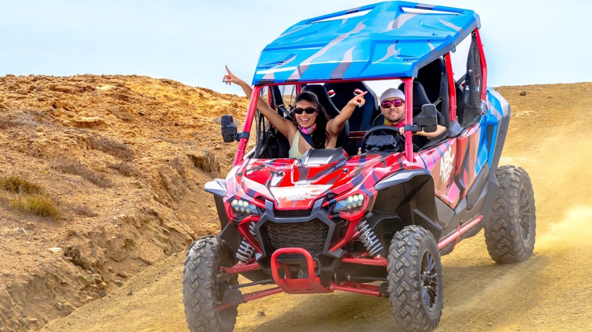 Two people in a colorful off-road vehicle driving on a dirt path.