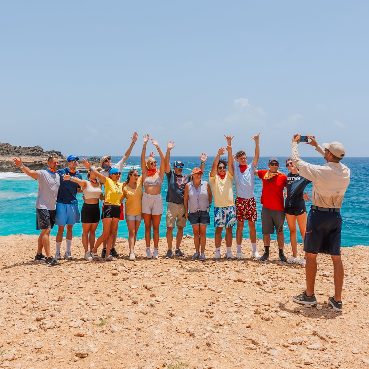 Group of people posing by the ocean, arms up, sunny day.