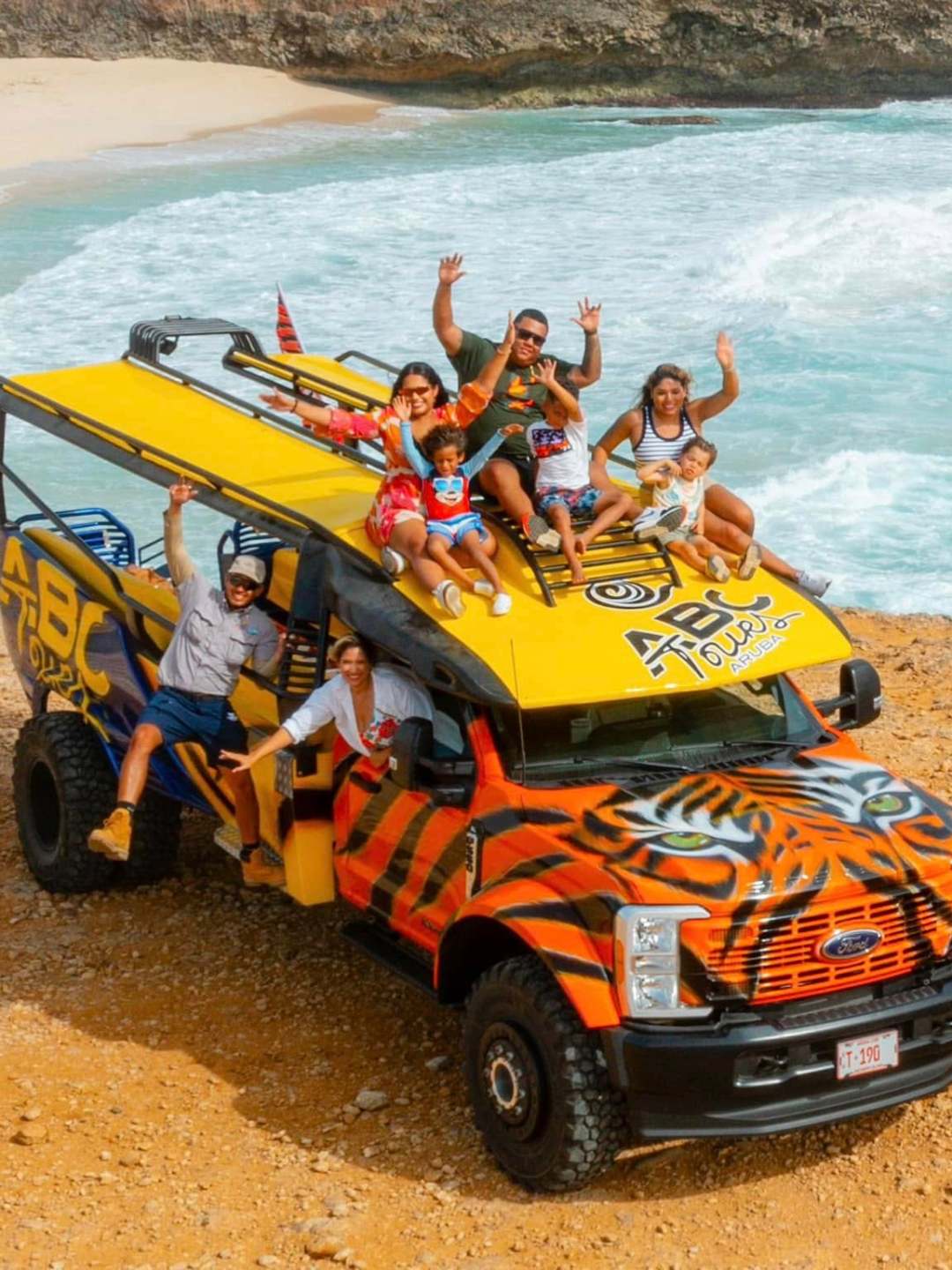 Group of people on a colorful tour bus by the beach, waving and smiling.