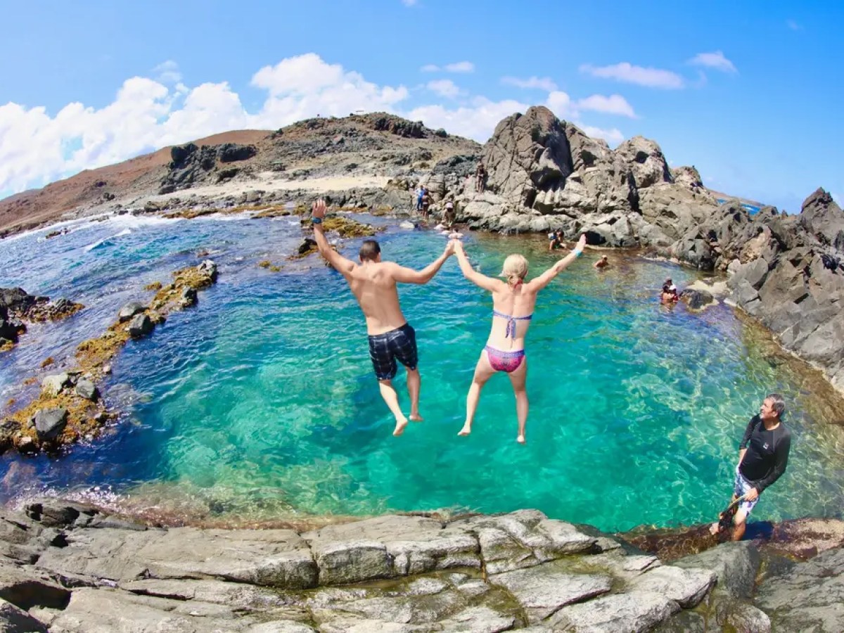 Two people jumping into a natural pool surrounded by rocks.