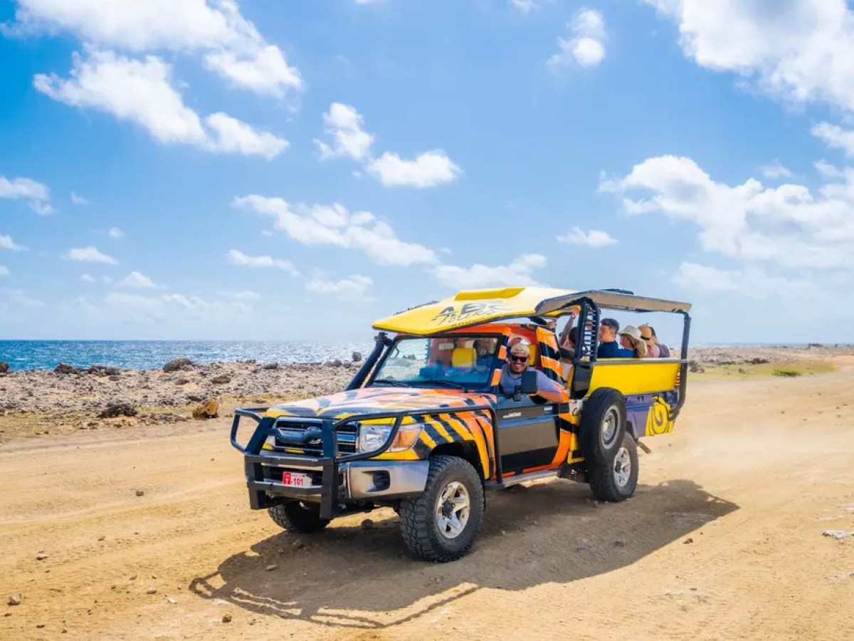 Off-road vehicle on coastal dirt road with passengers under blue sky.