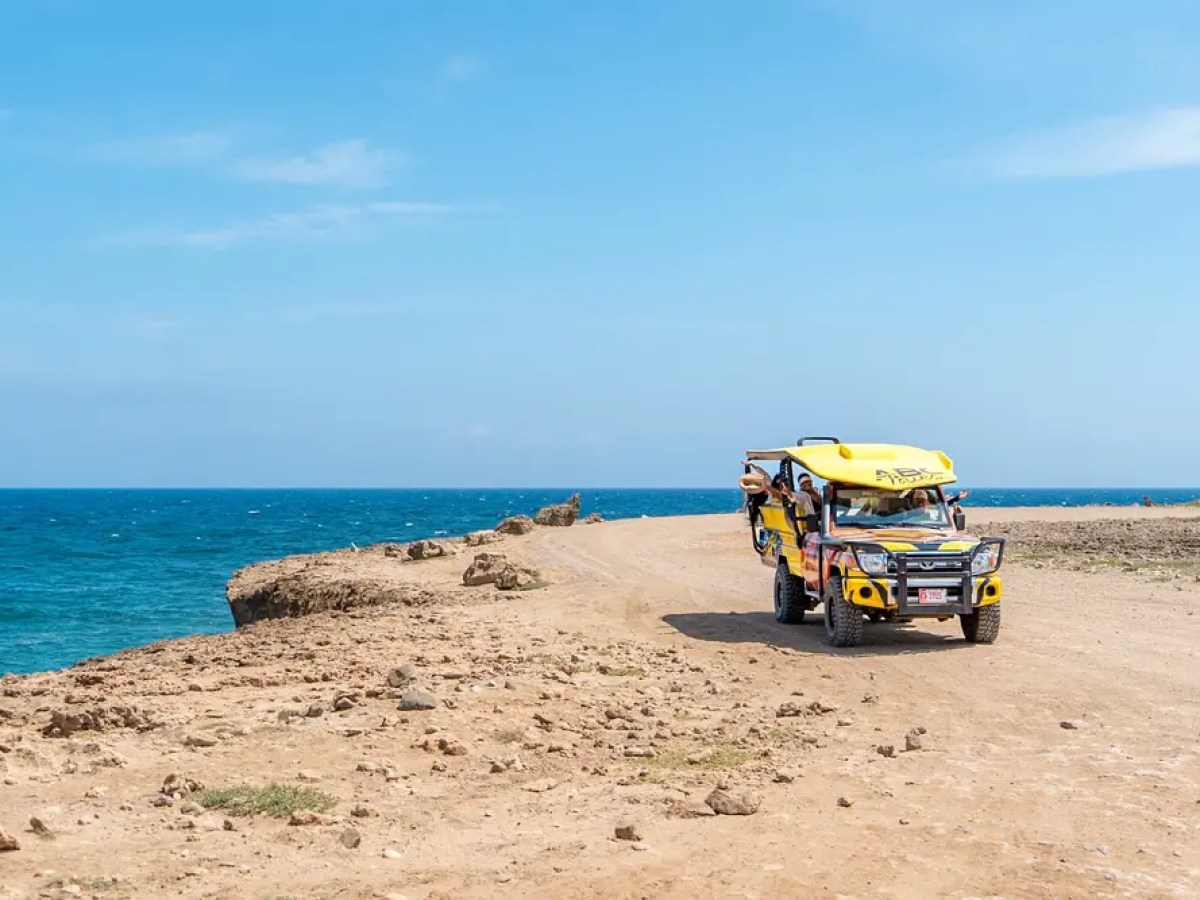 Jeep on coastal dirt road with ocean view and clear sky.