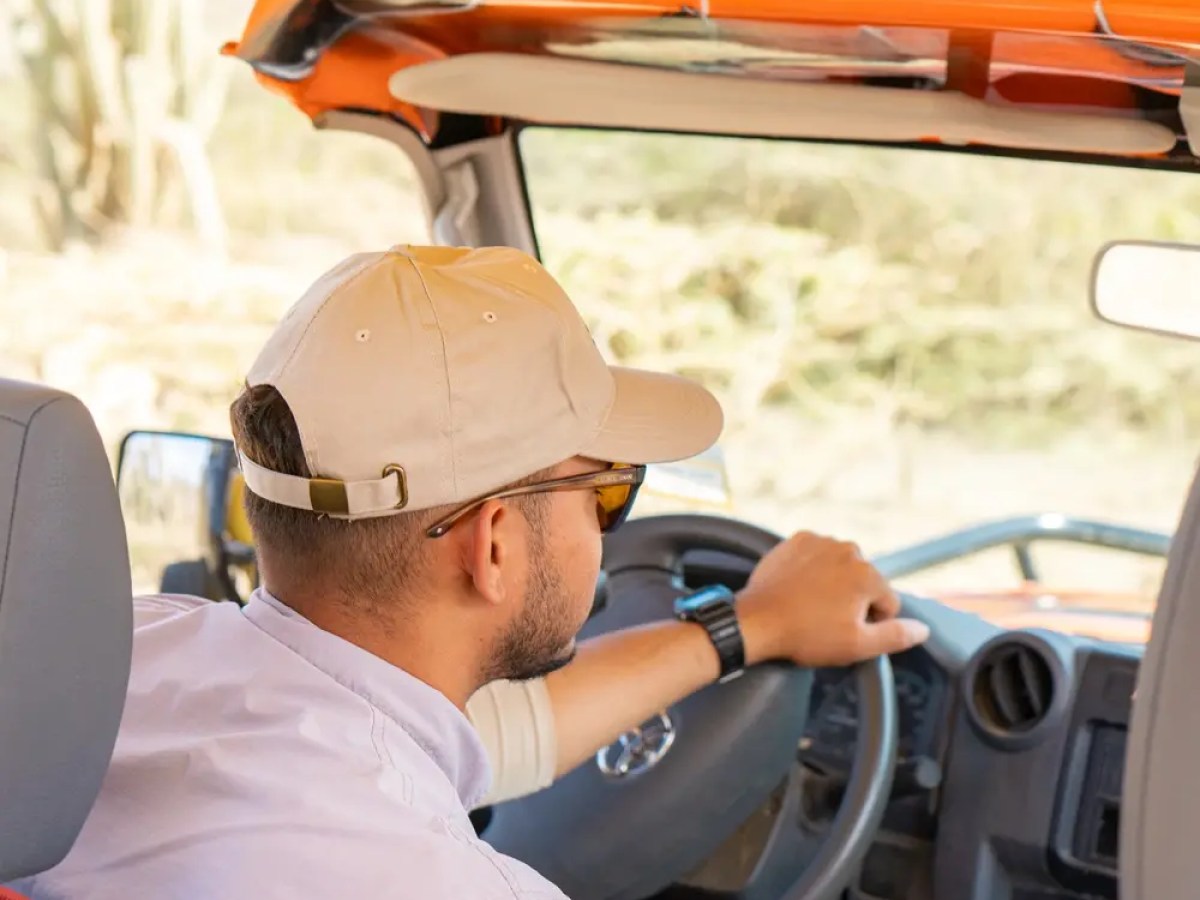 Person driving an open-sided vehicle, wearing a cap and sunglasses.