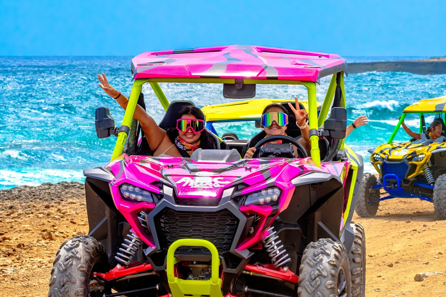 Bright pink ABC Tours Aruba UTV with another colorful UTV beside the sea